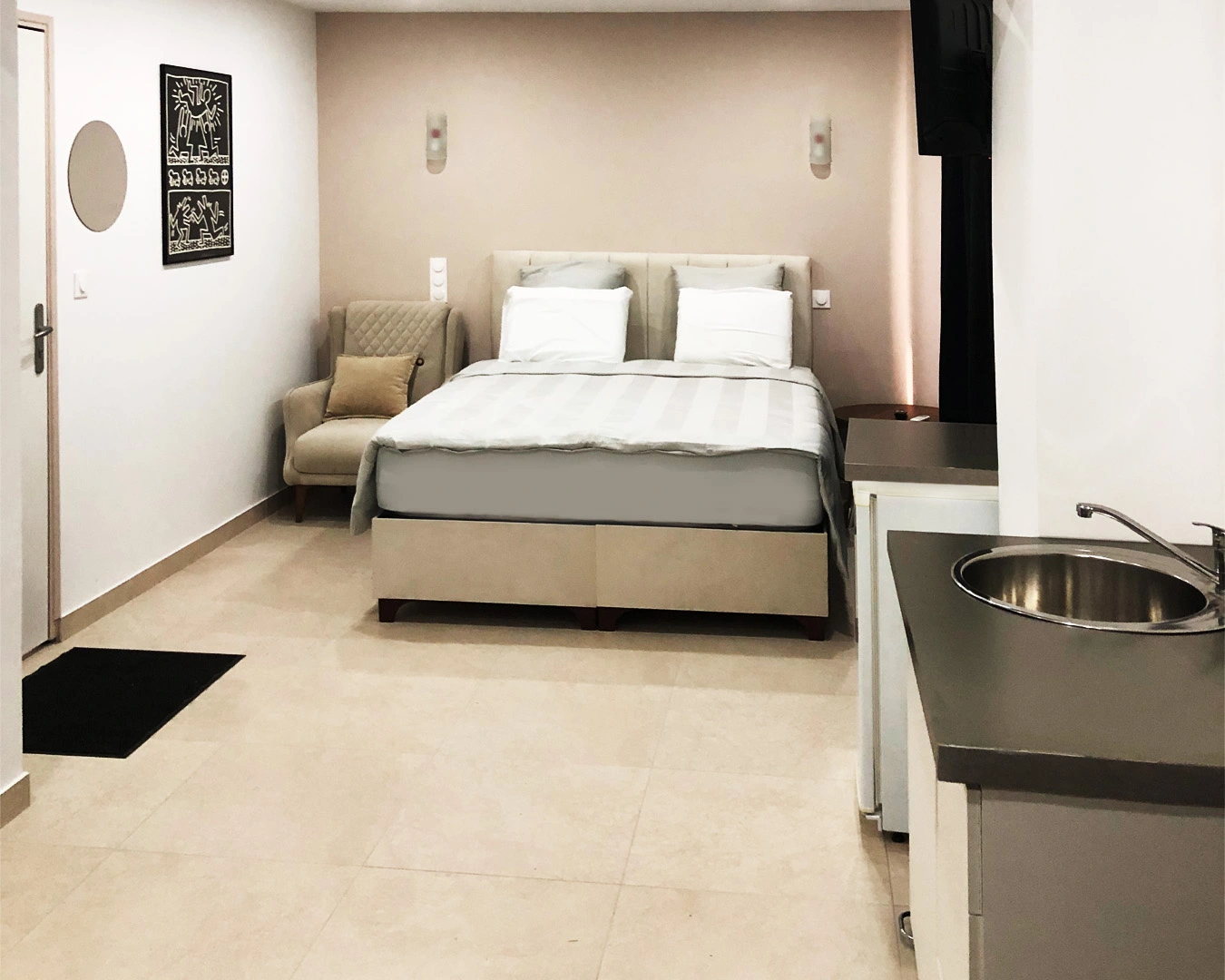 Notre chambre spacieuse et élégamment aménagée vous offre tout le confort pour un séjour relaxant dans un coin calme de la Bourgogne Franche-Comté. Lit double confortable, fauteuil cosy, espace kitchenette avec évier, TV murale, et décoration moderne : un hébergement idéal pour les couples ou voyageurs de passage à Montbéliard, dans le Doubs.