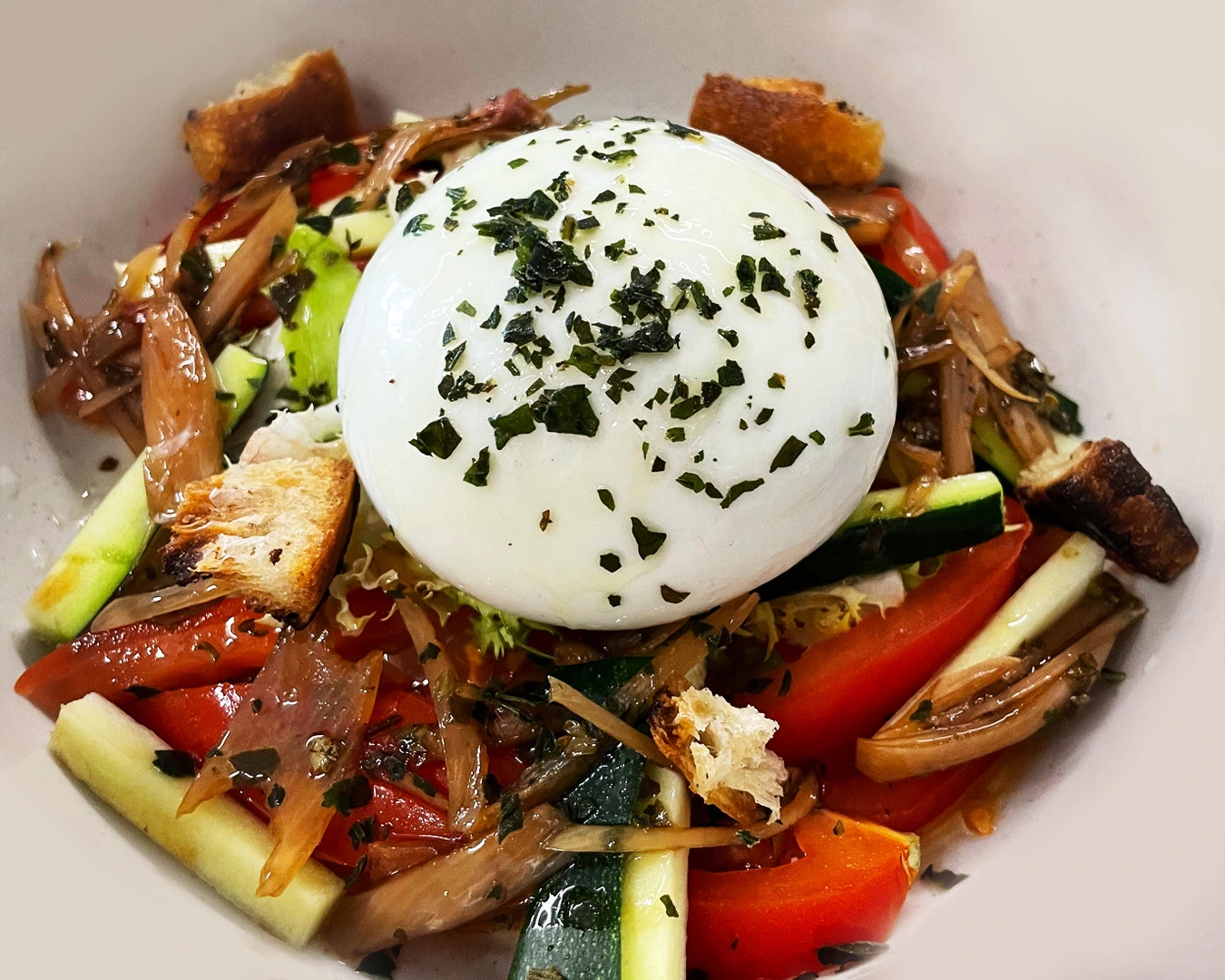 Assiette fraîche de burrata crémeuse sur lit de légumes croquants, tomates, courgettes, oignons confits et croûtons, servie dans une chambre d’hôtes à Montbéliard en Bourgogne Franche-comté.
