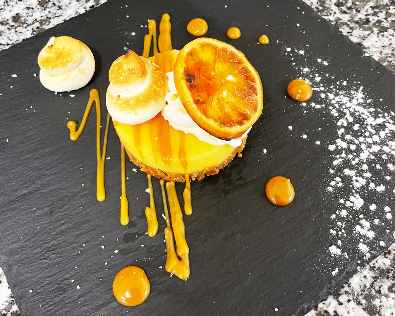 Tartelette citron meringuée revisitée avec zestes caramélisés, coulis d’orange et décor de meringues dorées, servie dans une chambre d’hôtes gastronomique à Montbéliard en Bourgogne Franche-comté.