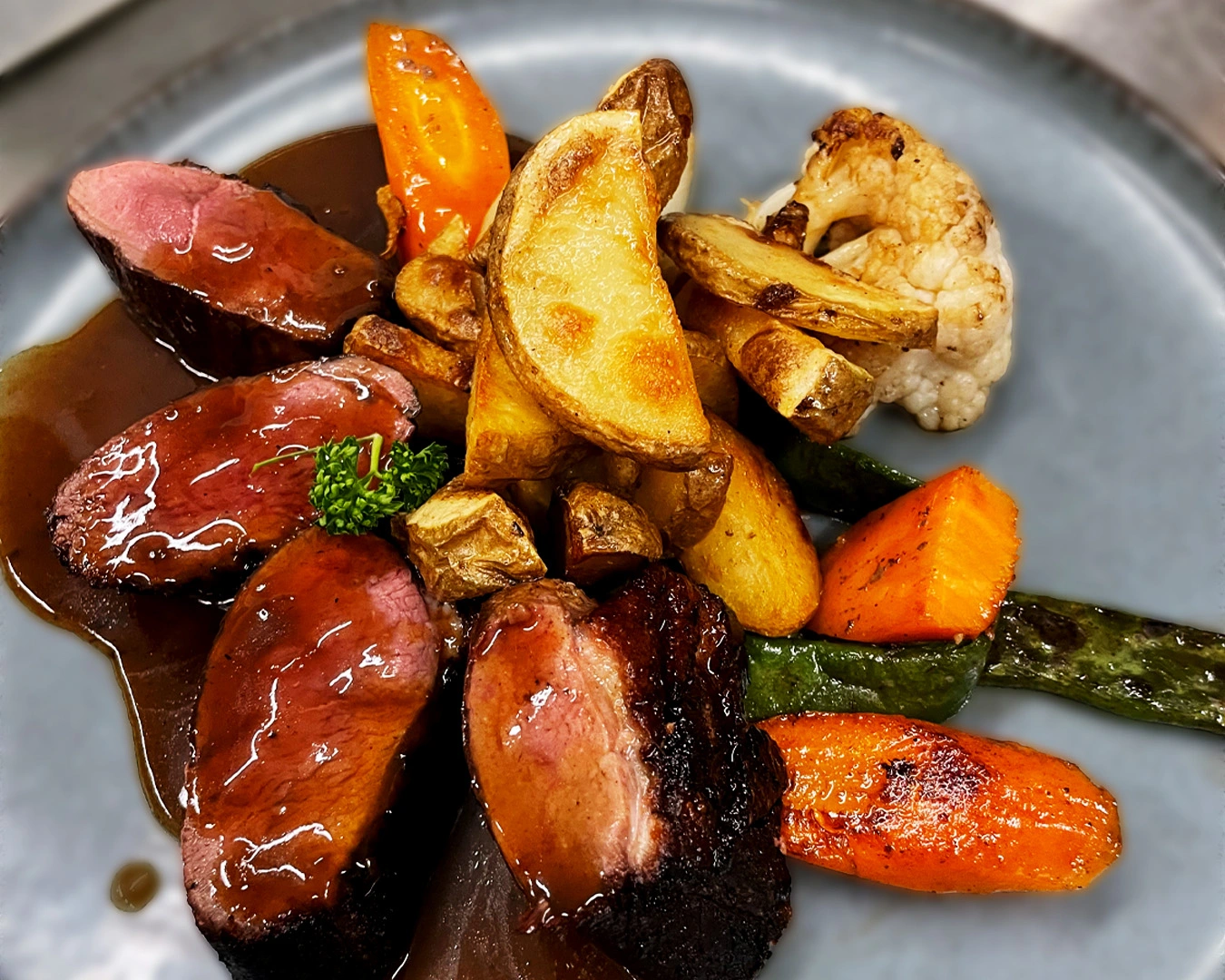 Magret de canard rosé nappé de sauce au vin, servi avec pommes de terre rôties, légumes de saison grillés (carottes, haricots verts, chou-fleur) – spécialité gastronomique dans un restaurant de Montbéliard en Franche-comté..