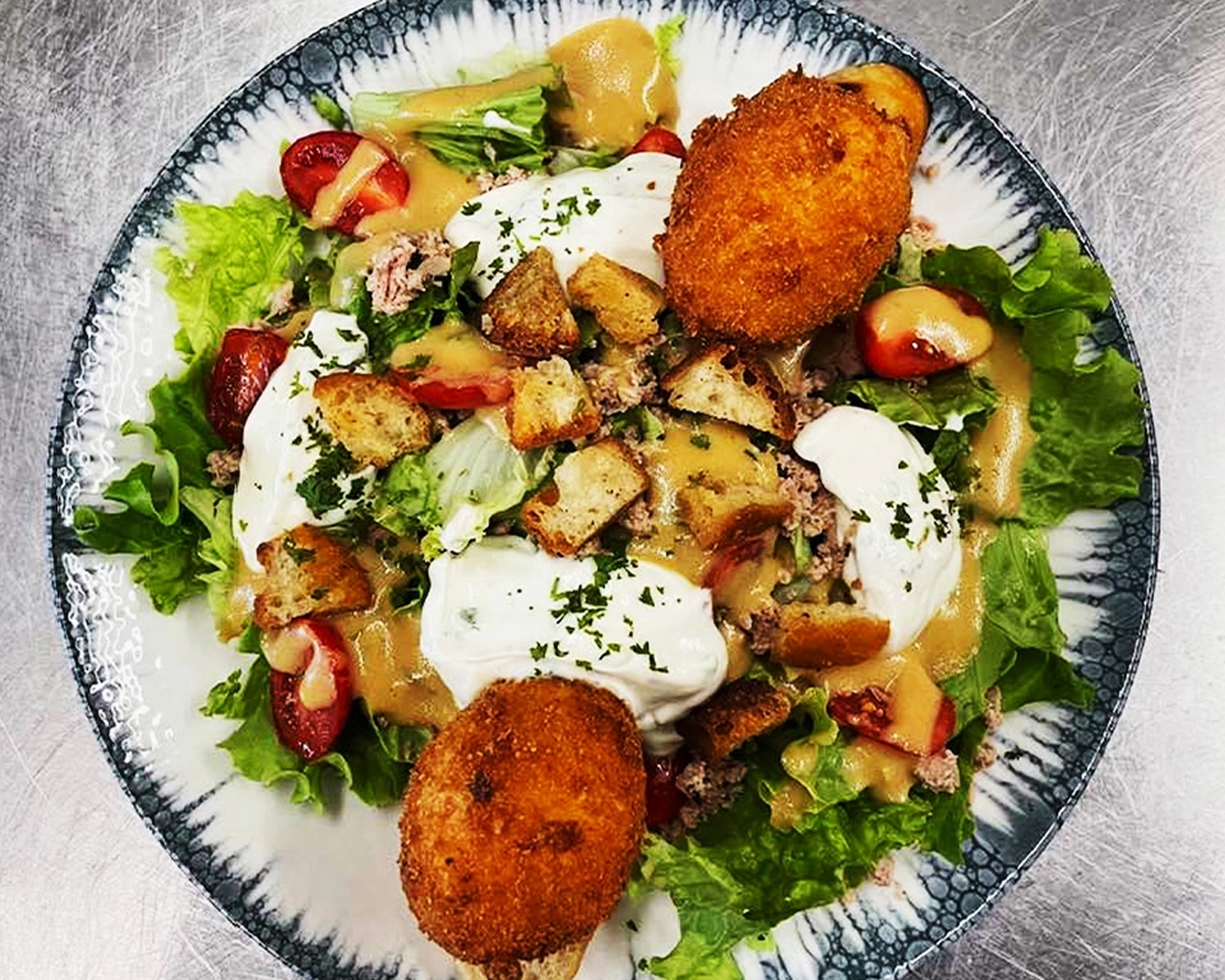 Salade gourmande servie dans un restaurant à Montbéliard, garnie de fromage pané croustillant, œufs pochés, croûtons maison, tomates cerises, laitue fraîche et vinaigrette maison – plat frais et copieux en dans le Doubs en Bourgogne-Franche-Comté.