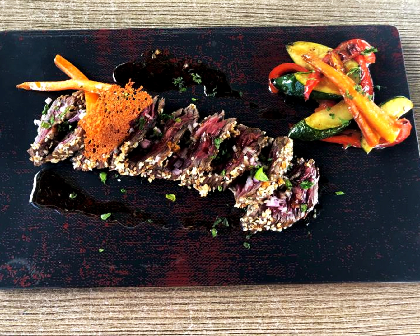 Tendre pièce de viande de bœuf grillée et enrobée de sésame, servie avec une sauce maison, légumes croquants de saison et chips croustillante, présentée avec élégance dans un restaurant gastronomique à Montbéliard en Bourgogne-Franche-Comté, reconnu pour sa cuisine créative et ses produits frais.